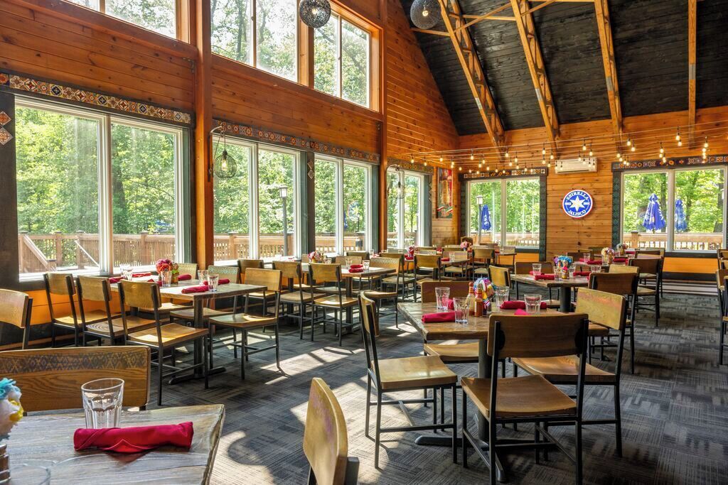 A spacious restaurant with wooden interiors, large windows, and a high ceiling.