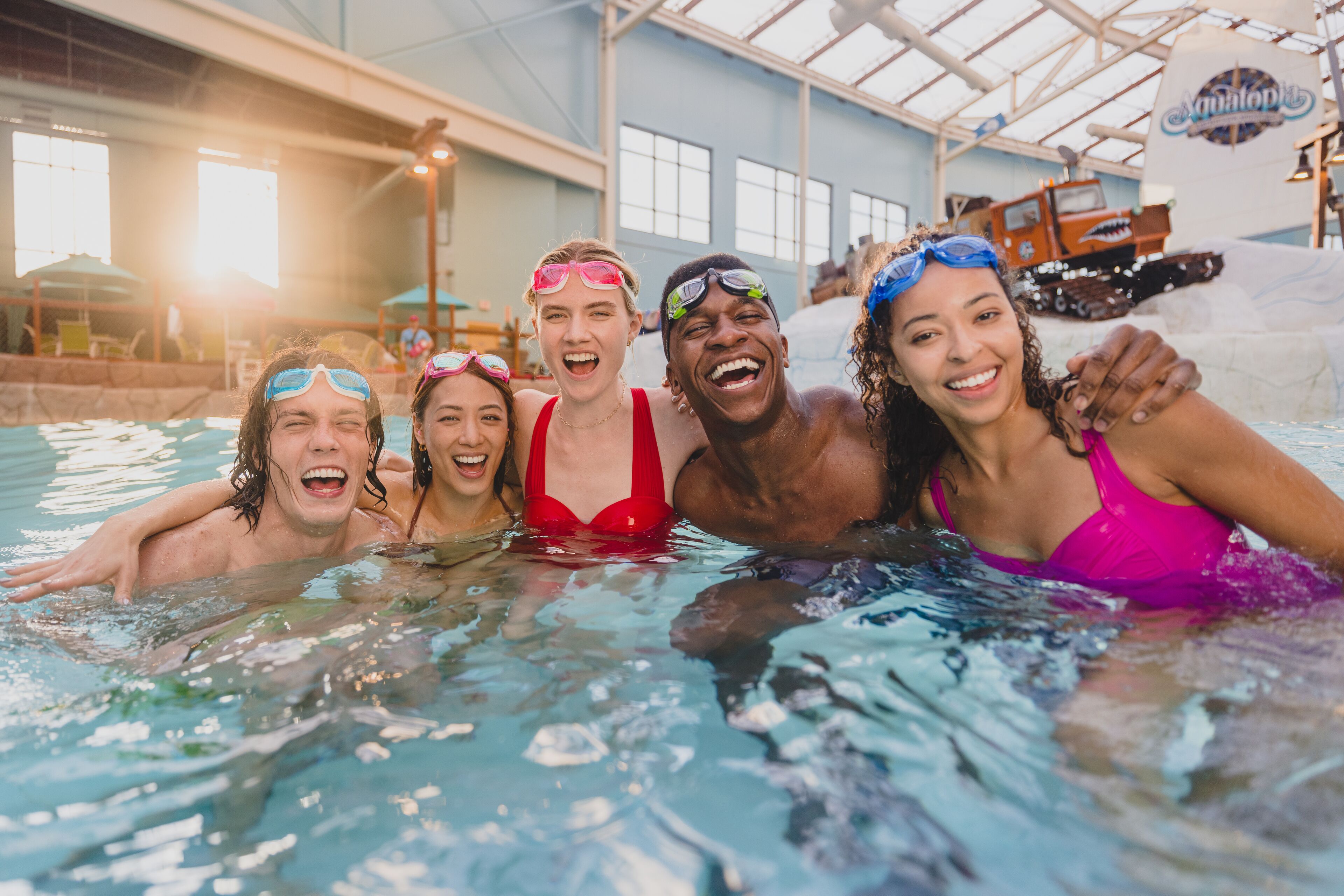 Eine Gruppe von Menschen in einem Schwimmbecken mit einer großen Wasserrutsche und einer Schiffswrack-Dekoration im Hintergrund.