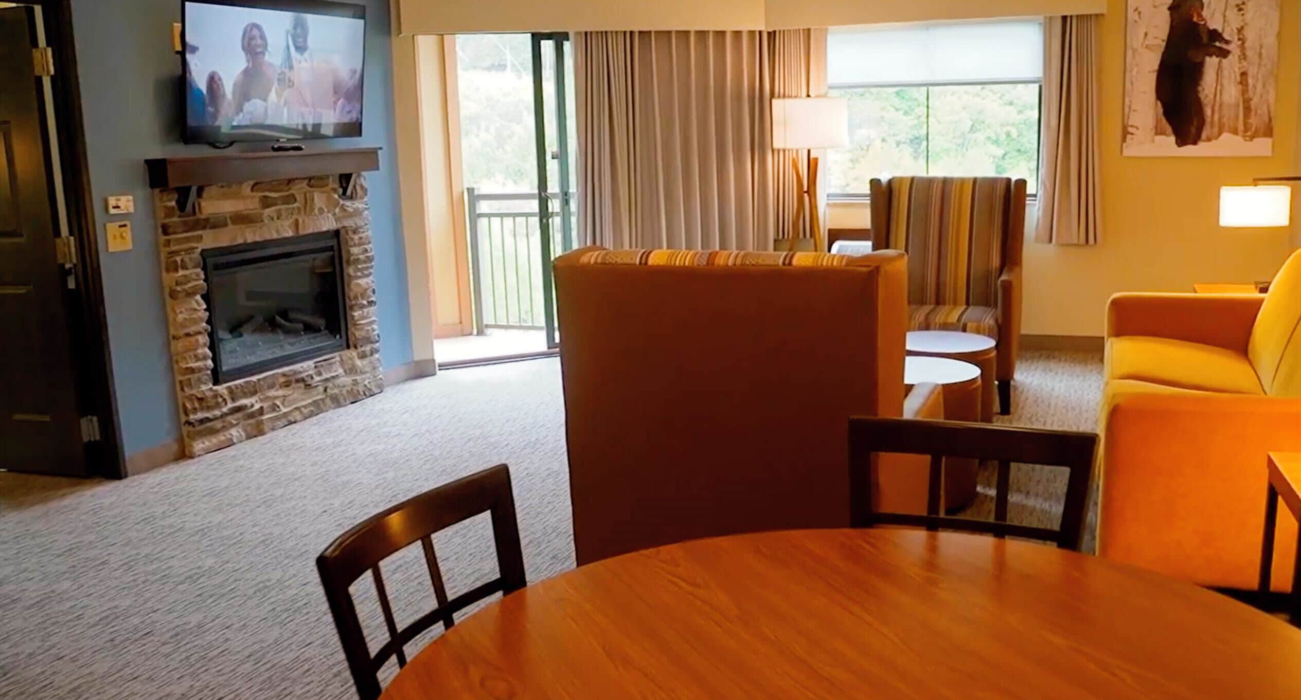 A living room with a stone fireplace, a television, a sofa, a yellow armchair, and a dining table.