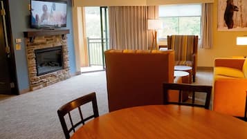 A living room with a stone fireplace, a television, a sofa, a yellow armchair, and a dining table.