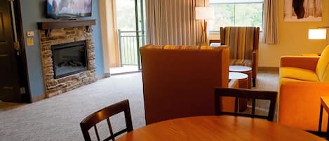 A living room with a stone fireplace, a television, a sofa, a yellow armchair, and a dining table.