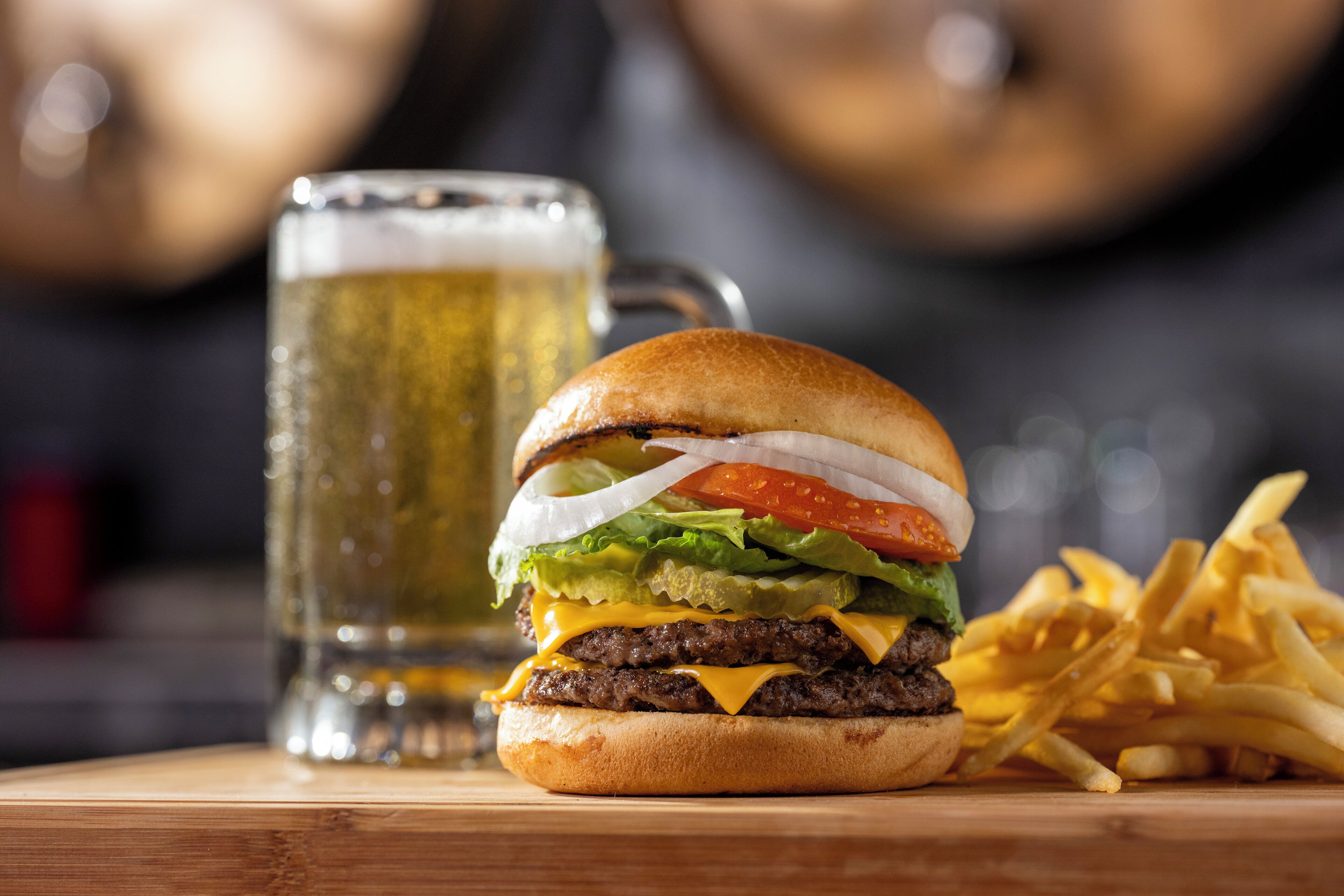 A burger with fries and a beer mug on a wooden table.