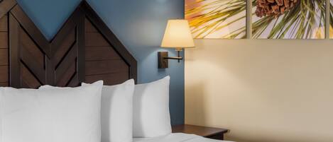 A neatly made bed with white linens and pillows, a wall-mounted lamp, and a pine cone decoration on the wall.