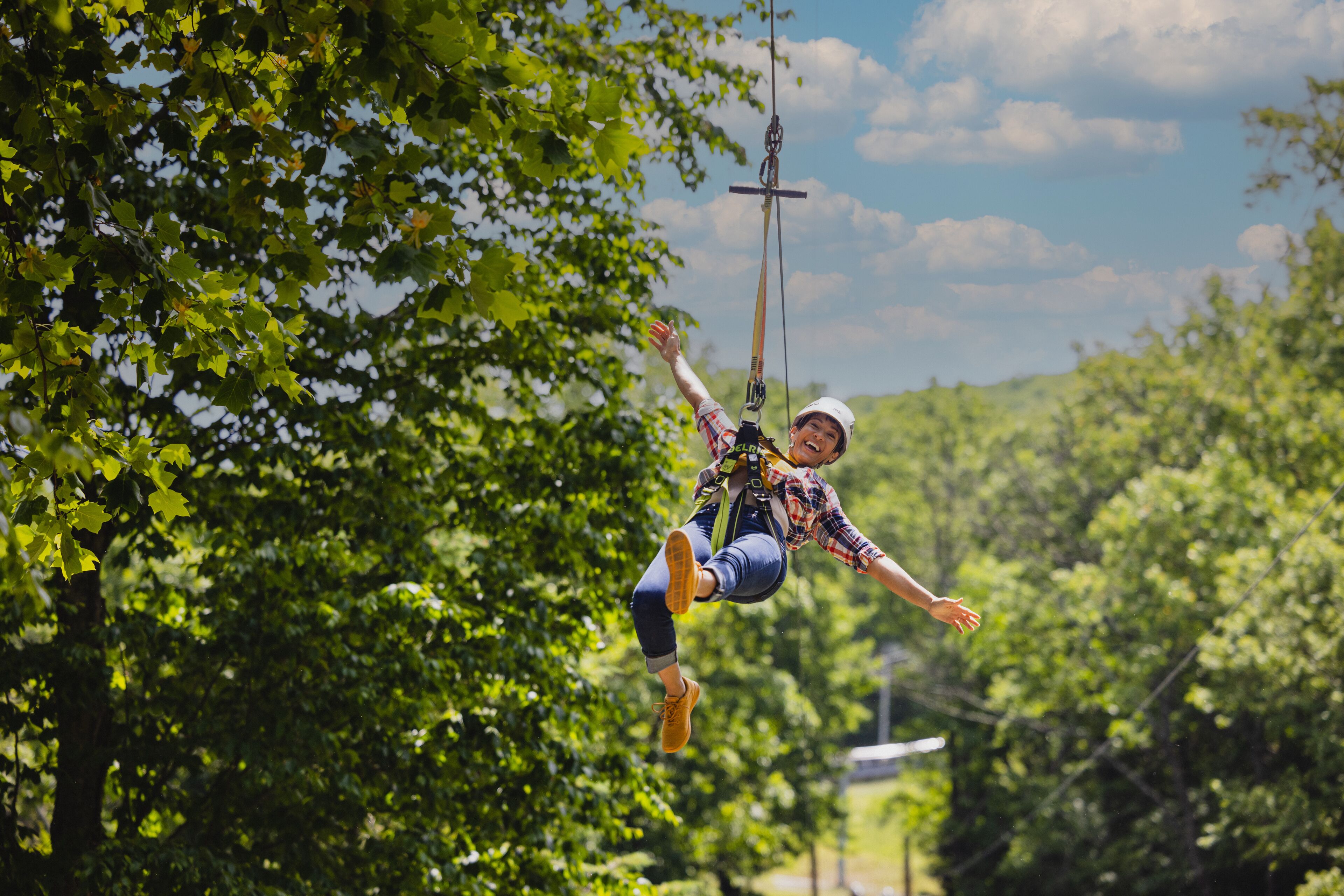 A person bungee jumping with a harness and safety gear, surrounded by lush green trees.