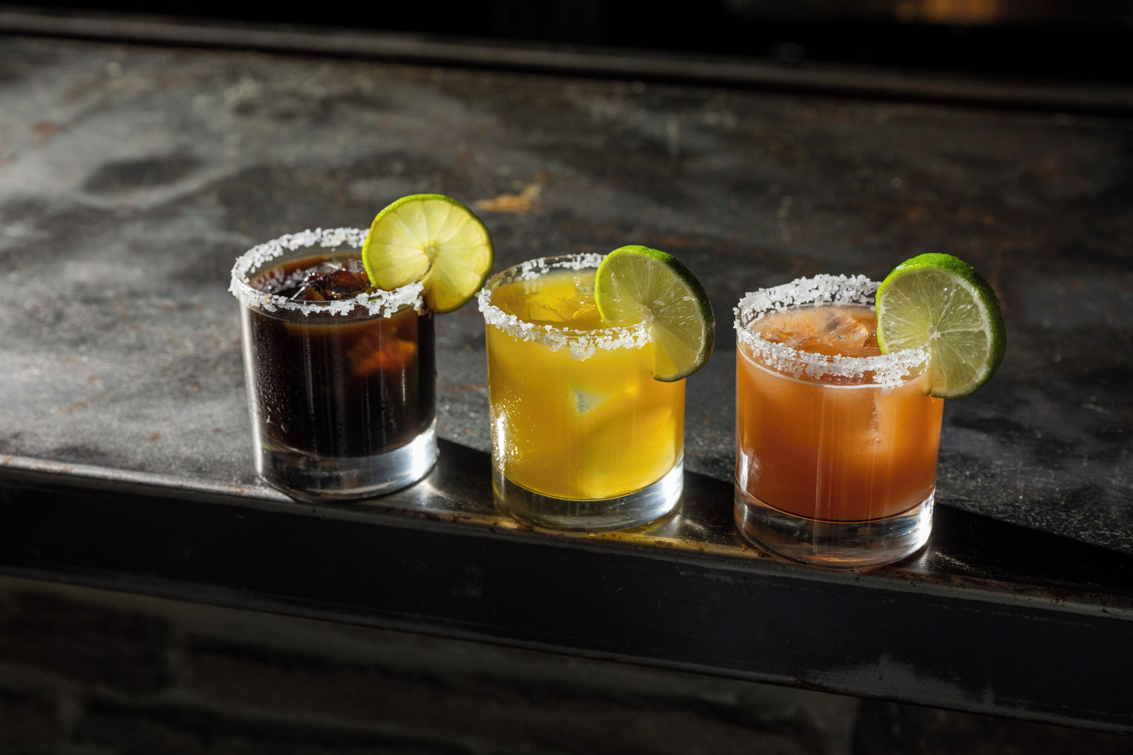 Three glasses of cocktails with lime garnishes on a bar counter.