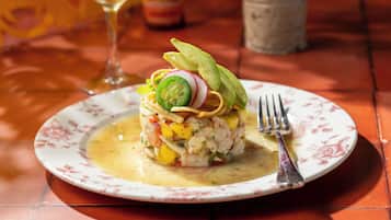 A plate of ceviche with avocado and radish on a floral plate, accompanied by a glass of white wine and a bottle in the background.