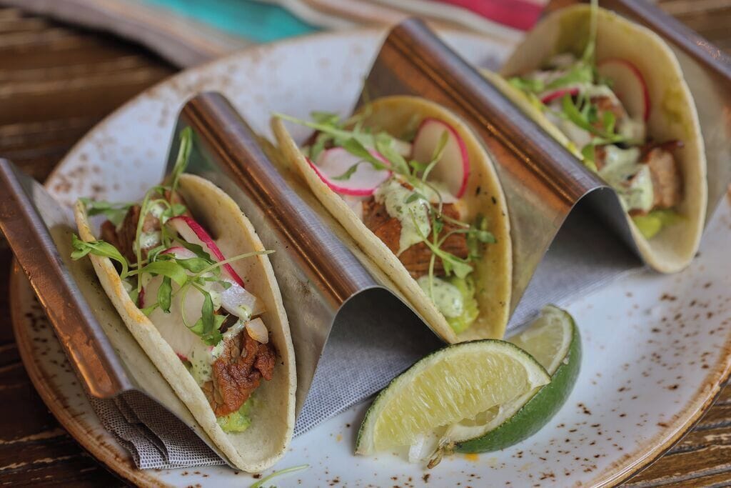 Drie taco's op een bord met een partje limoen.