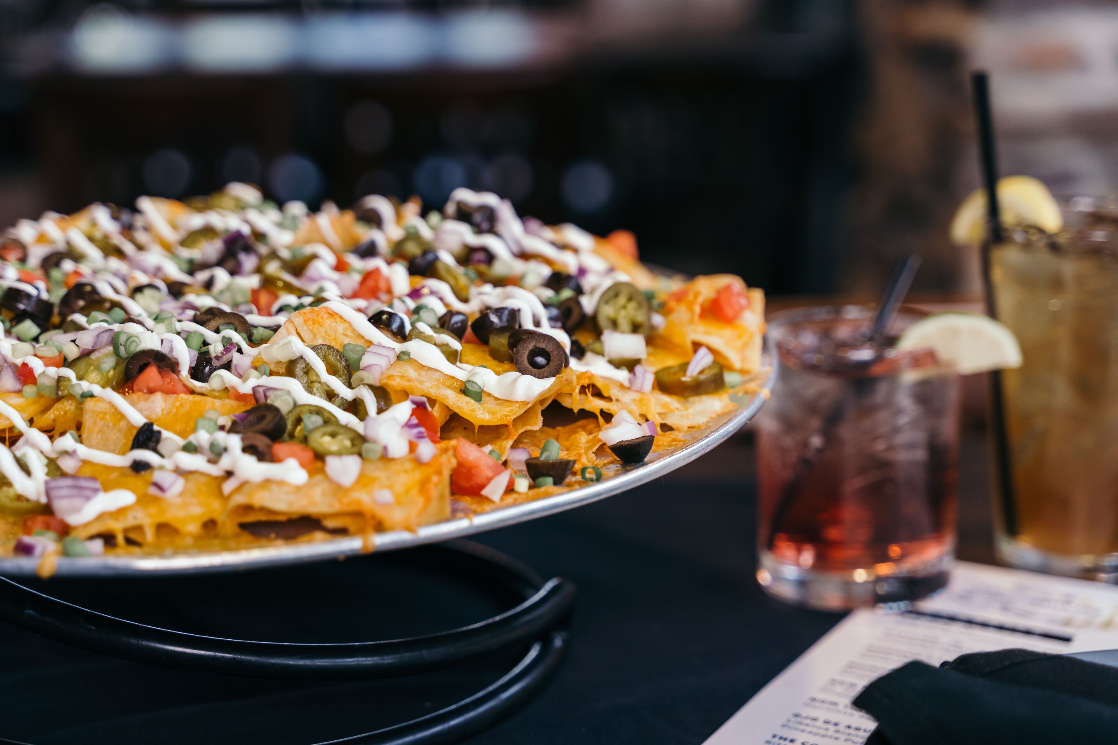 A large nacho dish with various toppings, a drink with a straw, and a menu on the table.