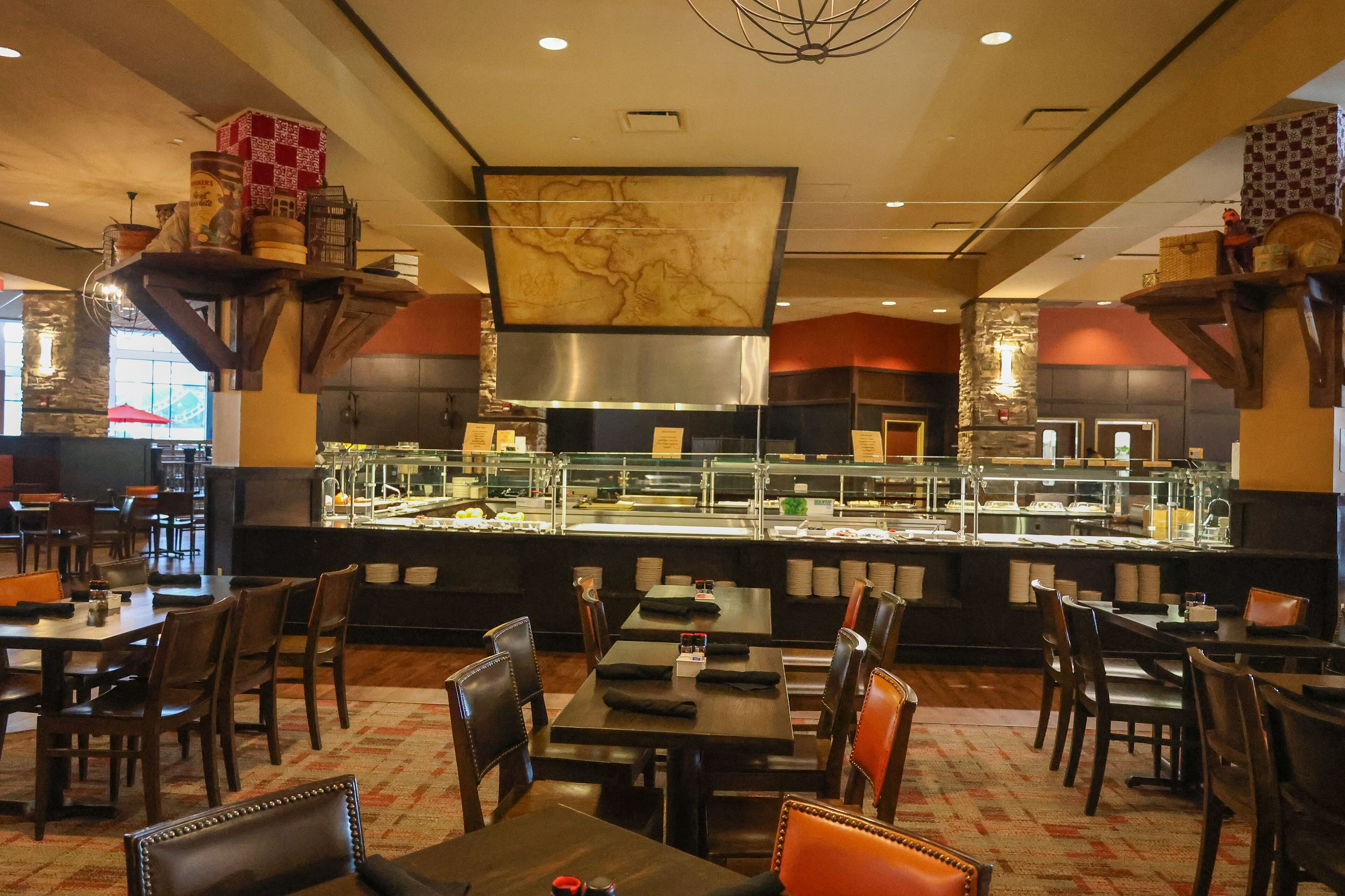 A restaurant with a buffet area, wooden tables and chairs, and a large decorative wall.