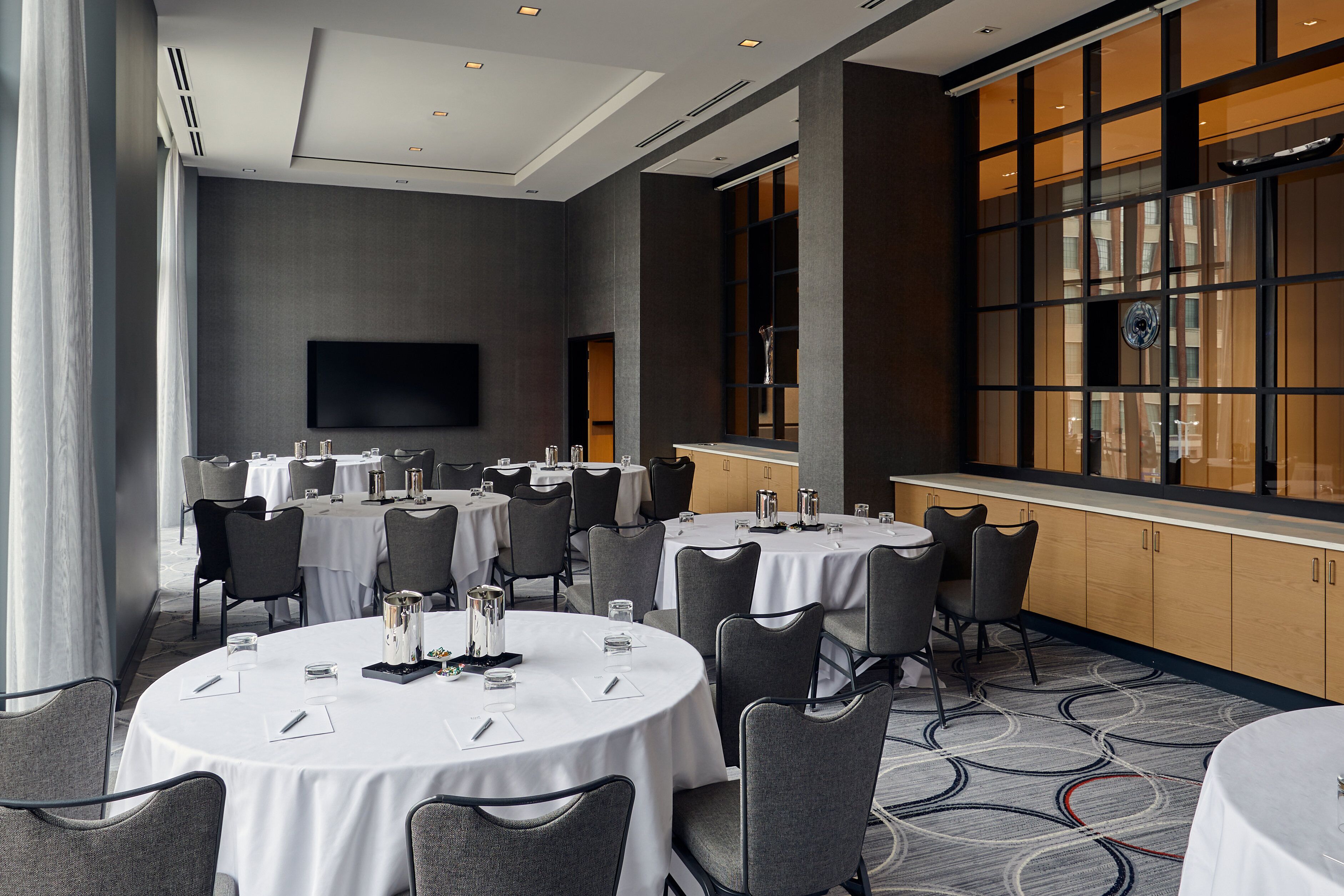 A conference room with multiple round tables, chairs, and a large screen.