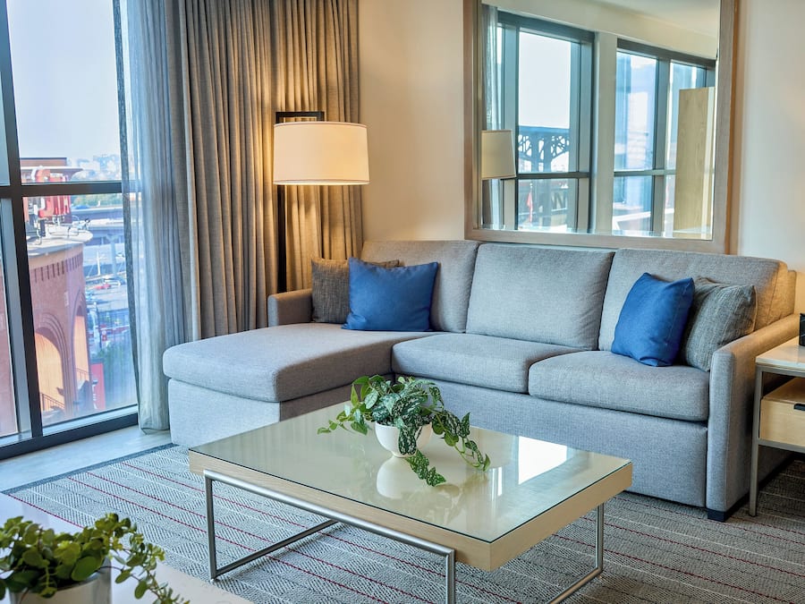 A modern living room with a grey sofa, blue cushions, a glass coffee table, and a potted plant.