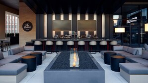 A modern bar area with a central fire feature, bar stools, and seating. - Live by Loews - St.Louis (St. Louis)