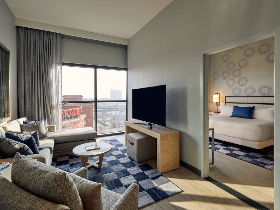 A modern hotel room with a sofa, a small coffee table, a TV, and a bed with a patterned headboard.