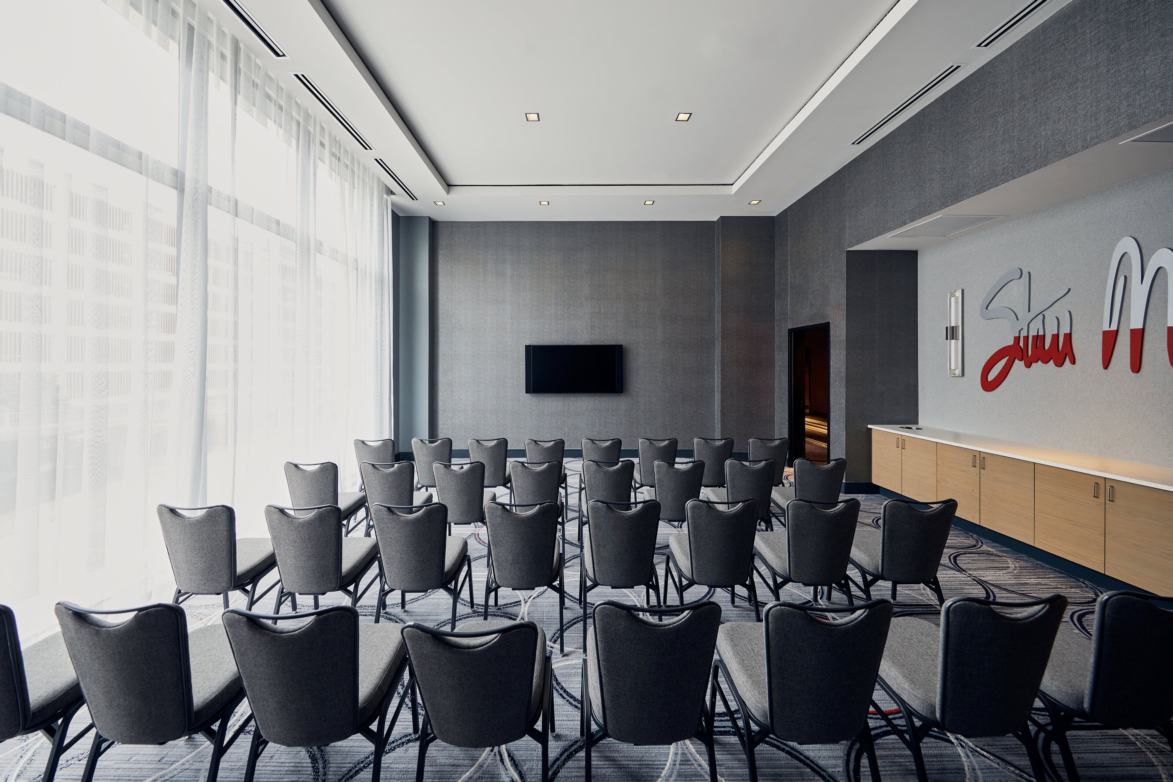 A conference room with rows of chairs facing a large screen, a reception desk, and a view of the city through large windows.