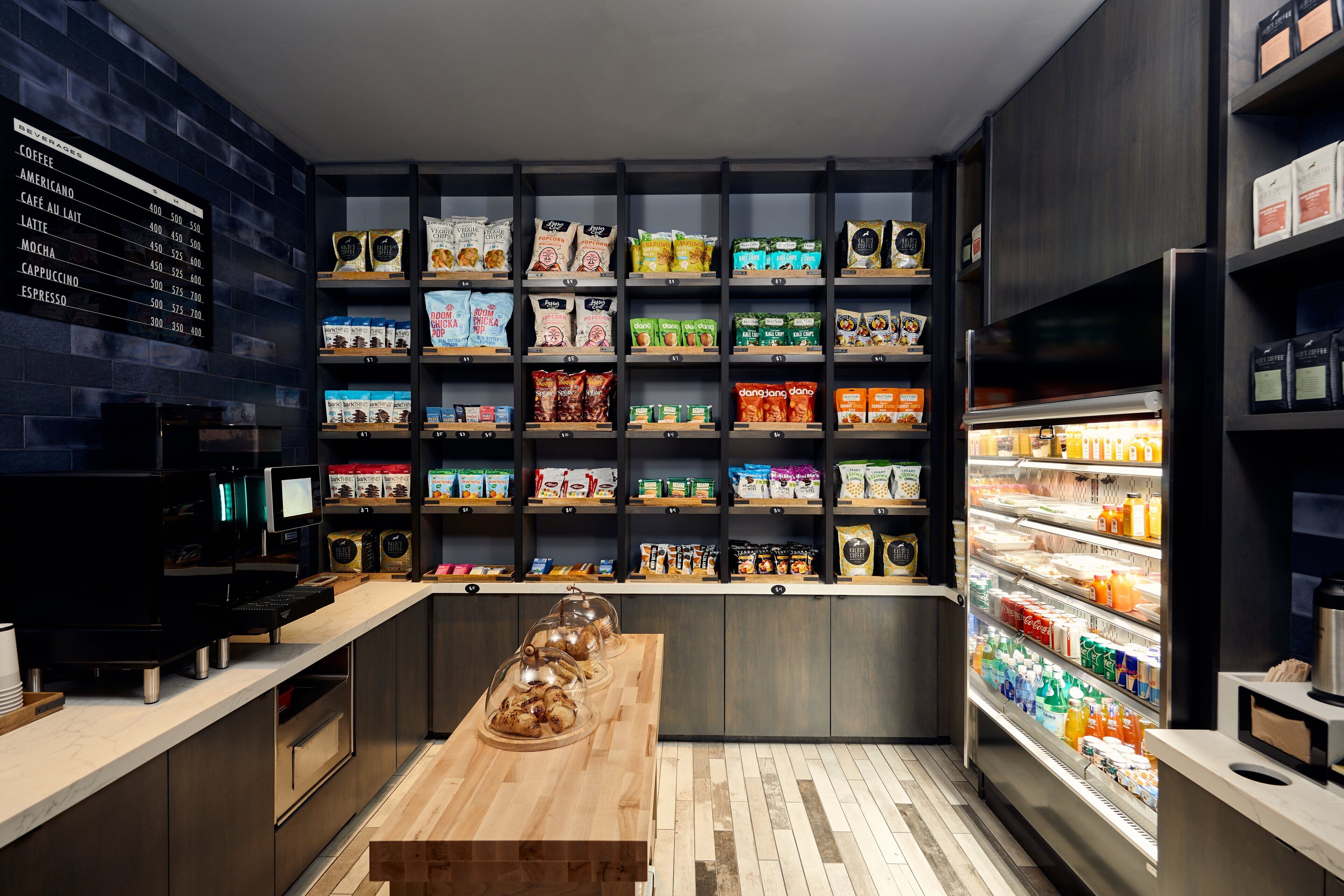 A modern coffee shop with a menu board, shelves of coffee beans, pastries, and a refrigerated display of beverages.