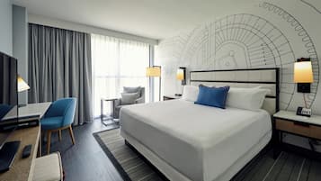 Habitación de hotel con una cama grande, un escritorio con silla, un televisor y una pared con un diseño circular.
