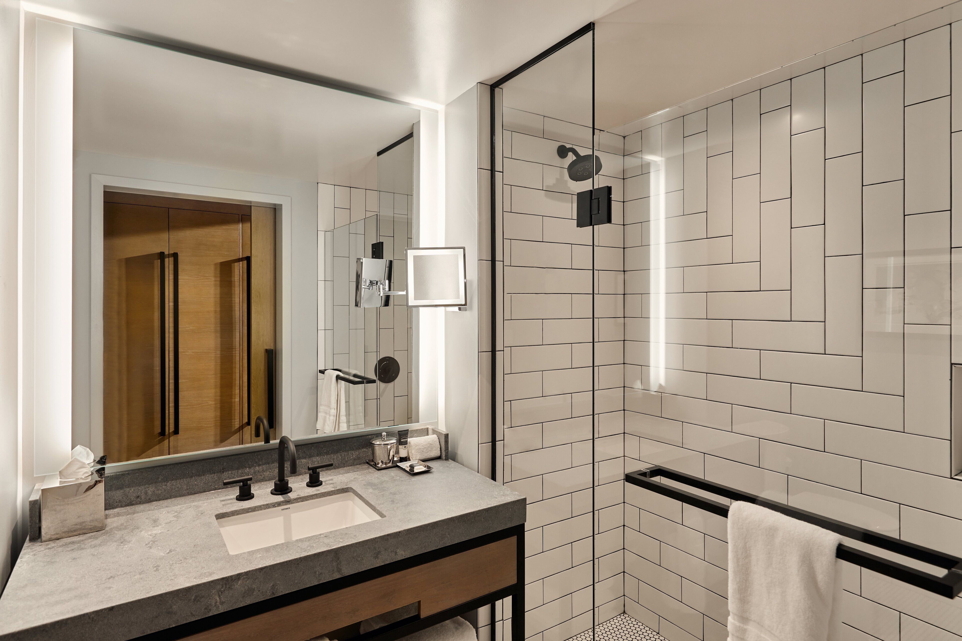 Un baño moderno con un espejo grande, un lavamanos, una ducha y un perchero para toallas.