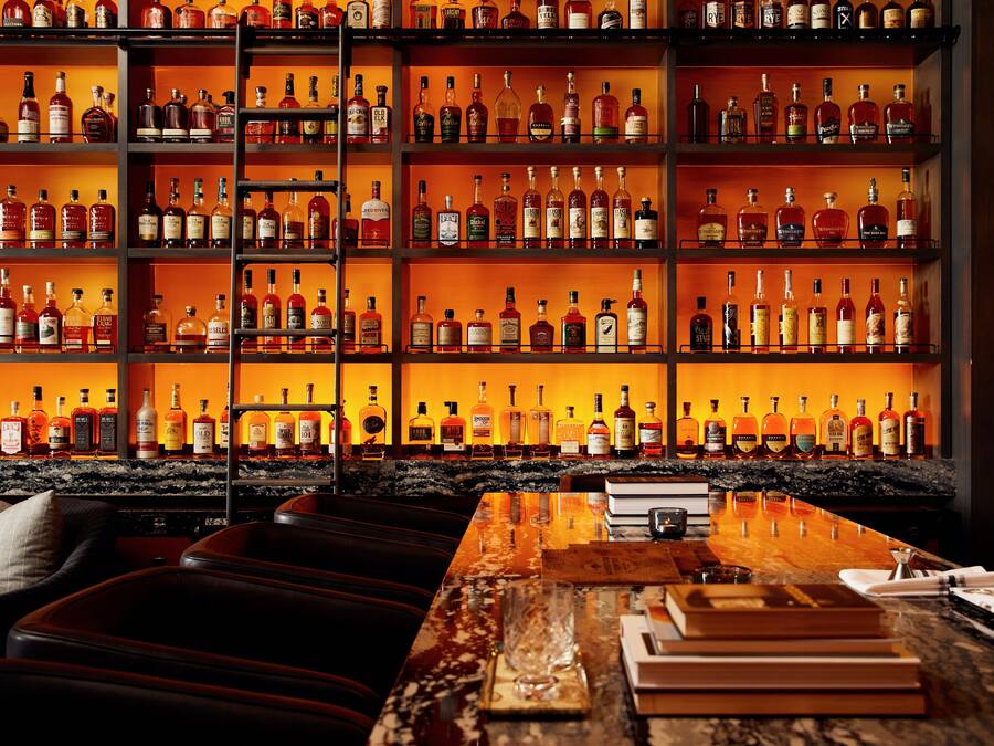 Un espace bar avec des étagères remplies de bouteilles d’alcool et un comptoir où l’on peut s’asseoir.