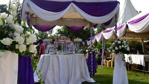 A tented outdoor wedding setup with a white table and purple drapes. - Scenic View Hotel & Resort (Nairobi)