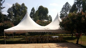 A covered outdoor seating area with tables and chairs, surrounded by a garden with trees and shrubs. - Scenic View Hotel & Resort (Nairobi)