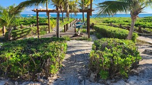 Un sendero de madera que lleva a una zona de playa con palmeras y una hamaca.
