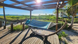 Una hamaca bajo una pérgola de madera con vista a la playa y al océano.