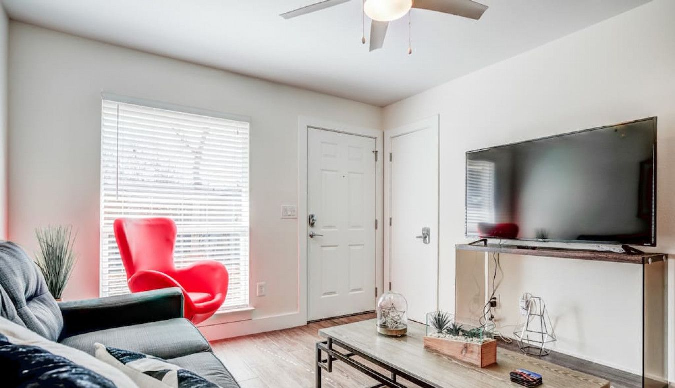 Un salon moderne avec un canapé, un fauteuil rouge, une table basse et un téléviseur fixé au mur.