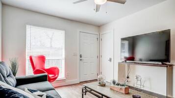 Un salon moderne avec un canapé, un fauteuil rouge, une table basse et un téléviseur fixé au mur.