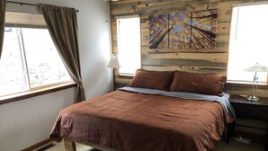 A bedroom with a wooden bed frame, a window with curtains, a nightstand, and a lamp. - This is your mountain getaway! (Lake George)