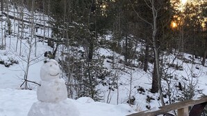 A snowman in a snowy outdoor setting with trees and a wooden fence in the foreground. - This is your mountain getaway! (Lake George)