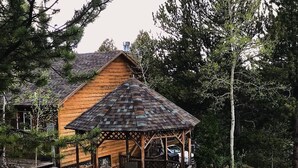 A wooden cabin with a gazebo, surrounded by trees and a rocky landscape. - This is your mountain getaway! (Lake George)