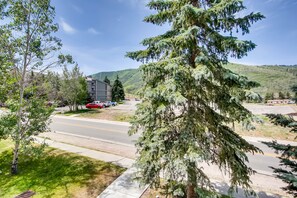 A residential street with a large evergreen tree, a multi-story building, and a clear blue sky. - Walk to Town Lift| Mountain View Balcony | Hot Tub| Managed by Park City Lodging (Park City)