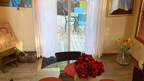 Een eethoek met een glazen tafel en stoelen, een vaas met rode bloemen en uitzicht op de omgeving door een glazen deur.