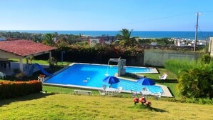 A residential area with a swimming pool, a view of the sea, and a red-roofed building.