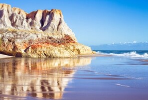 A beach with a rocky cliff and calm water reflecting the sky.