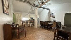 Un vaste espace de vie comprenant un piano, une table à manger avec des chaises, et une cuisine en arrière-plan.