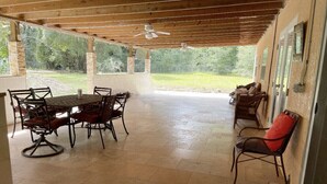 Une terrasse extérieure avec une table et des chaises en bois, un ventilateur de plafond et une vue sur la verdure environnante.