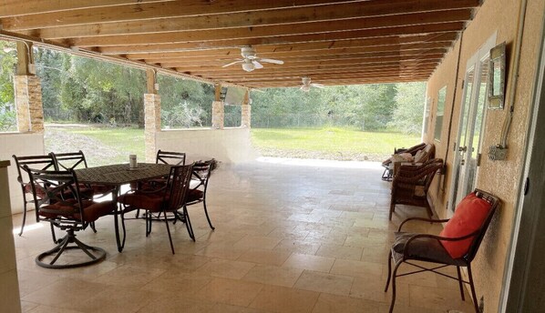 An outdoor patio with a wooden table and chairs, a ceiling fan, and a view of the surrounding greenery. - The Piano House Apopka (Apopka)