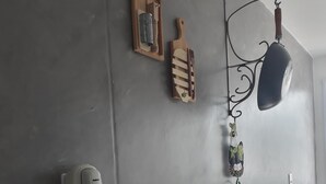 A kitchen wall with a white telephone, a hanging pot, a wooden cutting board with a grater, a wooden utensil holder, and a decorative hanging item.