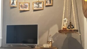 A room with a television on a wooden cabinet, a desk with a lamp, and a wall decorated with framed pictures and a hanging lantern.