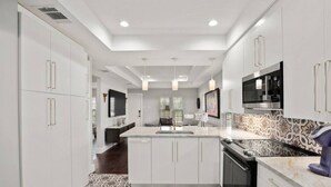 A modern kitchen with white cabinetry, a central island, a built-in oven, and a patterned backsplash. - Olander xxxxxxxxxxxx (Austin)
