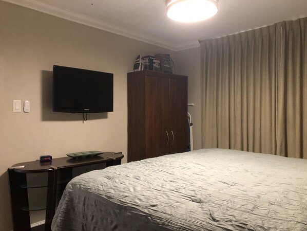 Una habitación de hotel con cama, televisor montado en la pared, escritorio con computadora y armario.