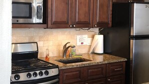 A kitchen with wooden cabinets, a stainless steel refrigerator, a microwave, a stove, and a sink with a paper towel holder. - LONG TERM RENTAL ONLY- Oceanfront 1bed/1 bath condo (Daytona Beach Shores)