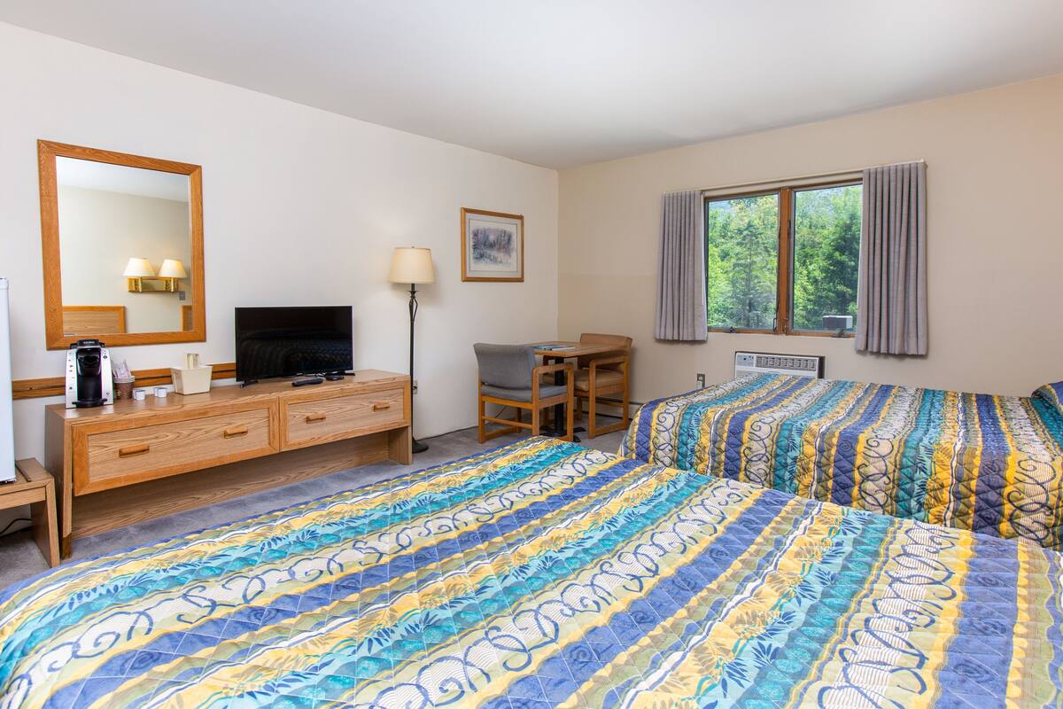 Ein Hotelzimmer mit Bett, Schreibtisch, Stuhl, Fernseher und einem Fenster mit Vorhängen.