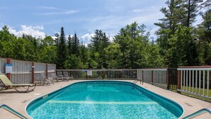 A rectangular swimming pool with a tiled edge, surrounded by a fenced deck area with lounge chairs and a covered seating area. - Mendon Mountainview Lodge (Killington)