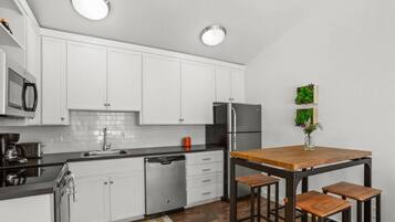 A modern kitchen with white cabinets, a stainless steel refrigerator, and a wooden island with bar stools.