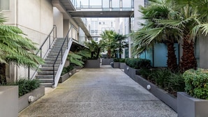 A modern building with a covered walkway, outdoor seating area, and various plants. - Mika, 2bdr Fitzroy pad With Secure Parking (Fitzroy)