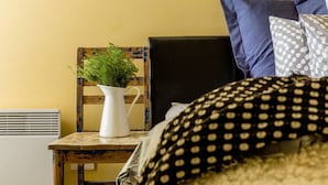 A room with a wooden chair, a white pitcher with green plants, a bed with a polka dot pillow, and a blue pillow. - Mika, 2bdr Fitzroy pad With Secure Parking (Fitzroy)