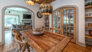 A rustic dining area with a wooden table, chairs, and a bowl of food. There are hanging pendant lights and a wooden ceiling. - A REAL Fixer Upper - Giraffe House (Waco)