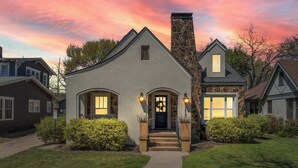 A single-story house with a stone chimney, a front entrance with a door, and two lit windows. - A REAL Fixer Upper - Giraffe House (Waco)